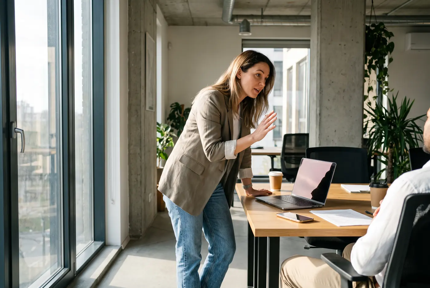A woman explaining something at a desk with a laptop and a phone